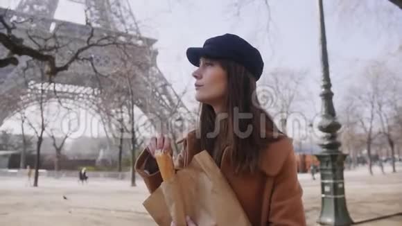美丽幸福的欧洲旅游妇女漫步在巴黎埃菲尔铁塔微笑吃新鲜法国风笛慢动作视频的预览图