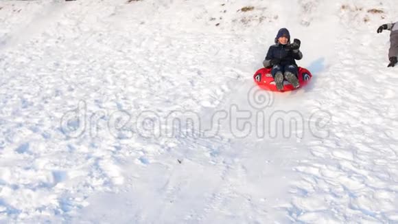 一个孩子在雪山上骑马和玩耍慢动作雪的冬季景观户外运动视频的预览图
