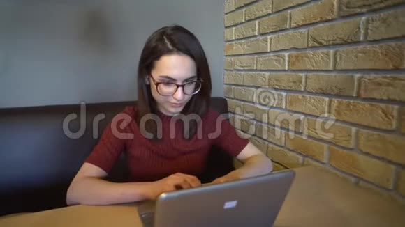 一个年轻的女人带着笔记本电脑坐在桌子旁一个女人拿着一台小笔记本电脑坐在家里写字视频的预览图
