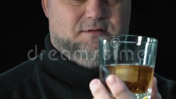大胡子男人喝威士忌加冰块孤立于黑色背景特写肖像酗酒和酗酒视频的预览图
