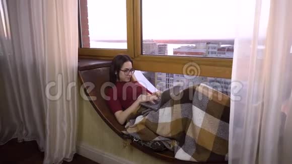 一个年轻的女人正在笔记本电脑上打字一个女孩躺在窗边的窗台上手里拿着一台笔记本电脑在外面视频的预览图