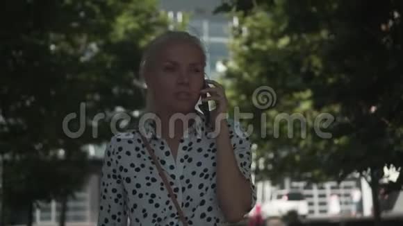 商务女性穿着一件白色衬衫带着豆在电话里说话背景是办公楼和绿树视频的预览图