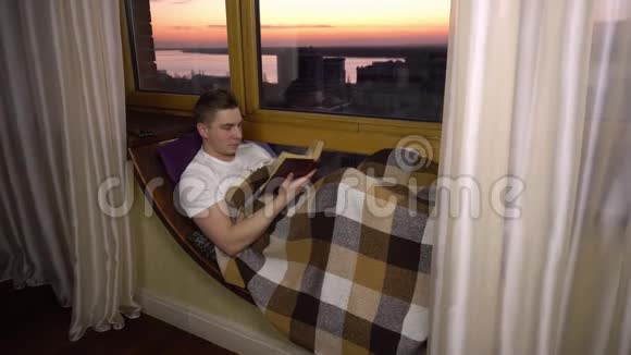 一个年轻人正在看书一个人躺在窗边的窗台上手里拿着一本书晚上出去视频的预览图
