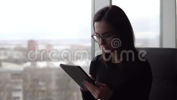 一个带着药片的年轻女人一个女孩坐在全景窗旁的咖啡馆里手里拿着一块平板电脑从视频的预览图