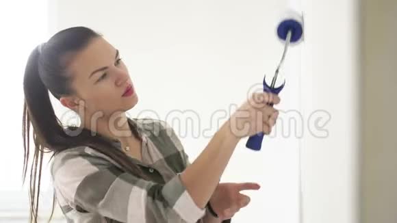 一个年轻美丽的女人在家画墙的肖像用滚筒工作公寓翻新视频的预览图