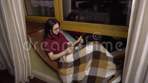 一个年轻的女人正在看书一个女孩躺在窗边的窗台上手里拿着一本书晚上出去视频的预览图
