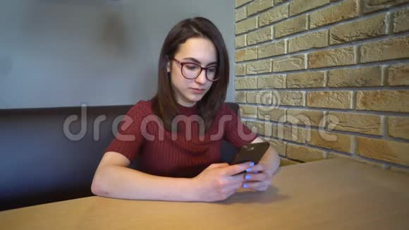 一个拿着电话的年轻女人坐在桌子旁一个女人坐在家里的一张桌子上拿着一部电话正在通信视频的预览图
