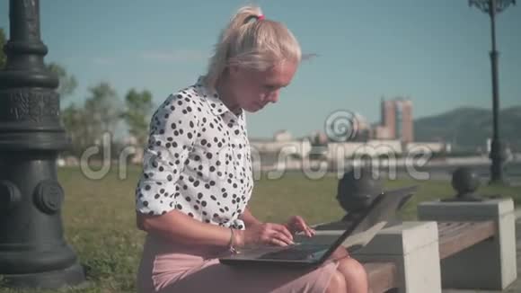 商务女性穿着白色衬衫黑豆坐在长凳上在笔记本电脑后面工作她工作很高兴视频的预览图