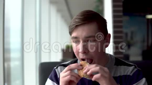 一个年轻人正在吃汉堡一个男人坐在全景窗旁的咖啡馆里吃快餐视频的预览图