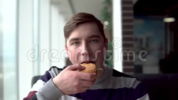 一个年轻人正在吃汉堡一个男人坐在全景窗旁的咖啡馆里吃快餐视频的预览图