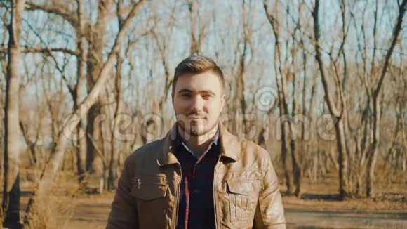 春天公园背景上穿皮夹克的人的肖像一个微笑的家伙正在享受即将到来的春天视频的预览图