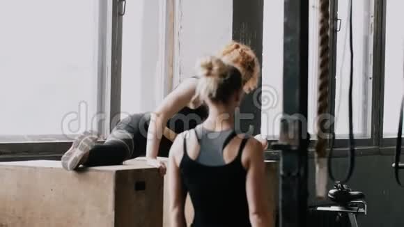 年轻漂亮的红头发女人做分裂伸展在瑜伽健身房金发个人教练拍照慢动作视频的预览图
