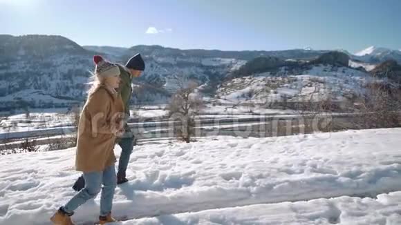年轻漂亮的夫妇走在雪道上背景是河和山晴天视频的预览图
