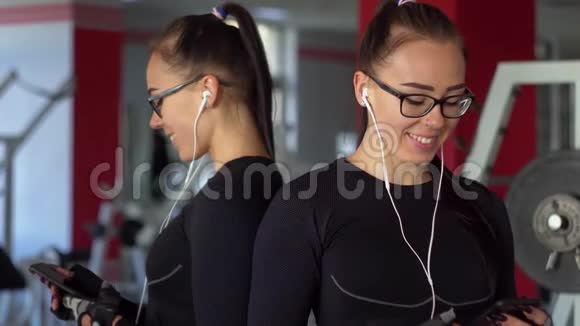 带着耳机的年轻女孩在健身房里用智能手机女孩听音乐视频的预览图