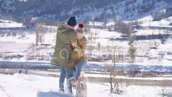 一对年轻漂亮的夫妇在一个阳光明媚的日子里和一只活泼的小狗在雪山上玩寒假概念视频的预览图