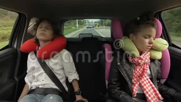 青少年男孩和女孩带着旅行枕头睡在汽车座椅上骑在后座兄妹旅行视频的预览图