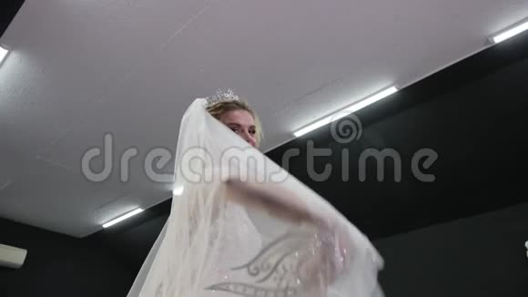 身穿白色婚纱头戴皇冠的金发新娘对着镜头抛面纱视频的预览图