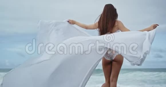 美丽的女士穿着漂亮的白色连衣裙在海边漫步她拿着她的长裙令人惊叹的海景视频的预览图