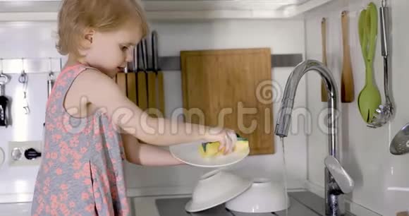 小女孩在厨房的水槽里用海绵洗碗视频的预览图