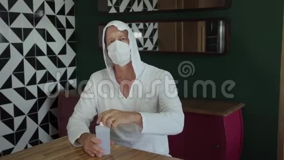 使用酒精凝胶成熟男人带防护面罩在家用消毒剂清洁双手视频的预览图