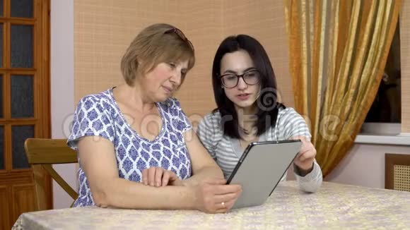 女儿教妈妈如何使用药片一个年轻的女人告诉她的老母亲在哪里点击平板电脑家庭视频的预览图