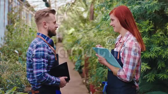 在一个大的温室里两个园丁在完成检查所有带红头发的植物女士后进行工作对话视频的预览图