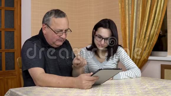 一个女儿教她父亲如何使用平板电脑一个年轻的女人向她的老父亲展示在平板电脑上点击的位置这就是视频的预览图