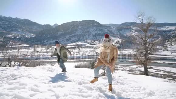 一对年轻漂亮的夫妇在一个阳光明媚的日子里在雪山上打雪球寒假概念视频的预览图
