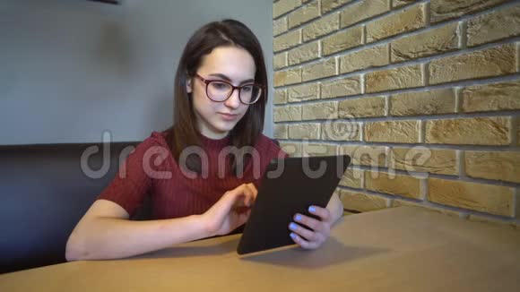 一个拿着平板电脑的年轻女人坐在桌子旁一个女人坐在家里的一张桌子上桌子上有一块平板电脑正在通信视频的预览图