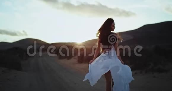 美丽的女士在日落时穿着一件白色的裙子在大自然的中心美丽的风景环绕着周围视频的预览图