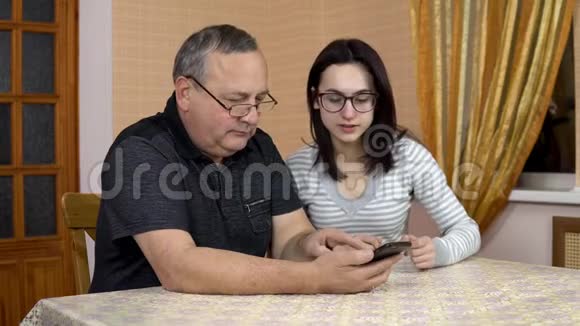 女儿教父亲如何使用电话一个年轻的女人告诉她的老父亲在哪里点击智能手机那个人视频的预览图