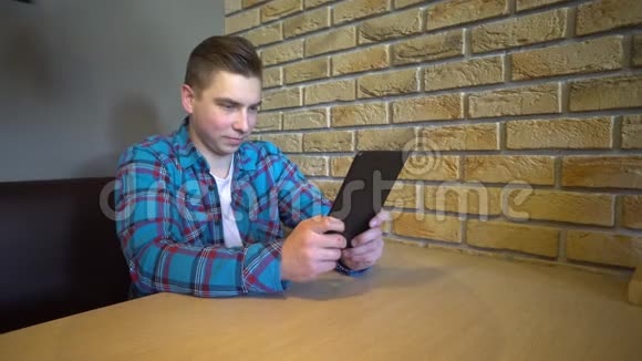 一个拿着写字板的年轻人坐在桌旁一个人坐在家里的桌子旁手里拿着一块写字板正在通信视频的预览图