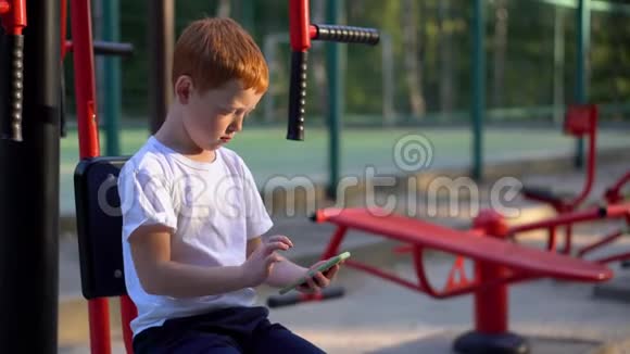 一个在街头公共健身器材上的男孩看着他的智能手机视频的预览图