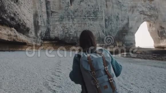 镜头跟随快乐的黑发旅游妇女步行到著名的白色拱门岩石沿海岸靠近埃特雷特缓慢的运动视频的预览图
