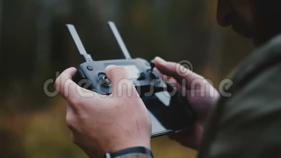 近距离后视镜男性手控制无人机飞机使用现代遥控器与智能手机在秋季森林视频的预览图