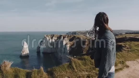 美丽的黑发女游客与相机走在美丽的海上海岸在埃特雷特头发吹在风中视频的预览图
