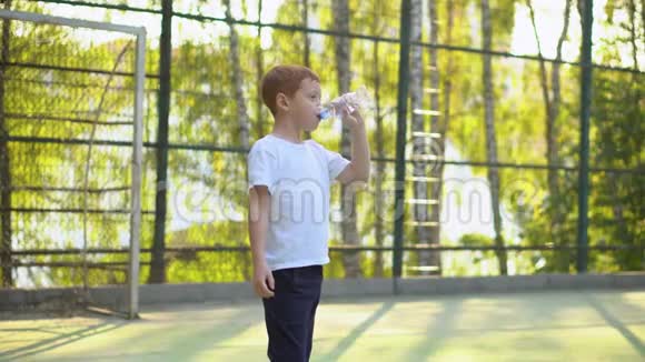 小男孩在室外公共足球设备附近饮水儿童运动视频的预览图