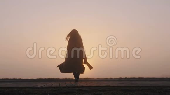 后景背景拍摄的快乐旅游女人带着相机行走到令人惊叹的粉红色雾状日落全景慢动作视频的预览图