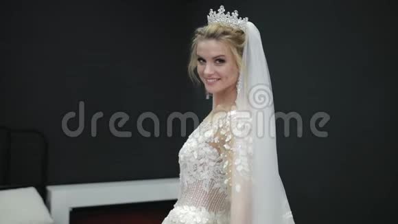 新娘穿着白色婚纱戴着面纱穿过房间黑墙微笑视频的预览图