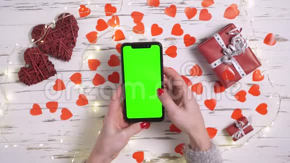俯视图女性双手使用智能手机在一张装饰有心脏的桌子上视频的预览图