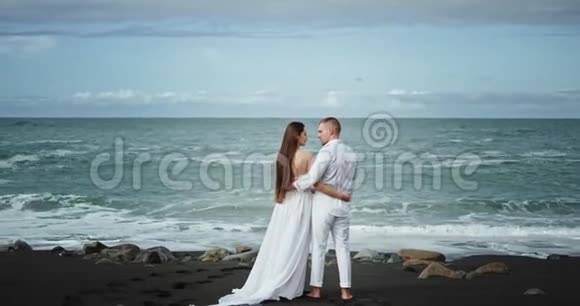 美丽的海滩边黑色的沙子站在海边令人惊奇的情侣相爱他们有一段浪漫的时光视频的预览图