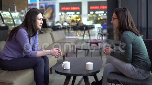 年轻的女人坐在咖啡馆里聊天妈妈和女儿坐在一起聊天喝咖啡视频的预览图