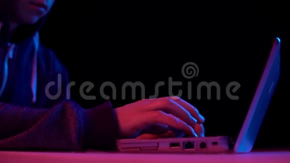 戴着笔记本电脑特写的青年黑客通过笔记本电脑进行黑客攻击蓝色和红色的光落在一个男人身上视频的预览图