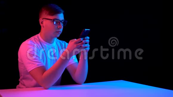 有智能手机的年轻人一个男人在用电话蓝色和红色的光落在黑色背景上的人身上视频的预览图