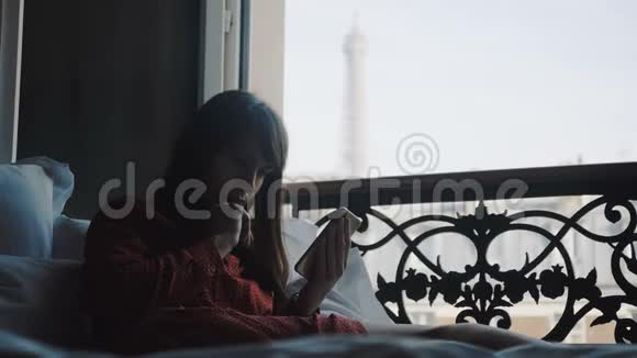 漂亮的成功女商人在法国阳台的床上使用智能手机应用程序埃菲尔铁塔景观慢动作视频的预览图