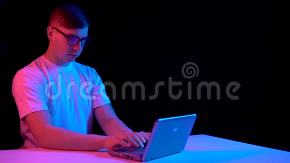 有笔记本电脑的年轻人男人用笔记本电脑蓝色和红色的光落在黑色背景上的人身上视频的预览图