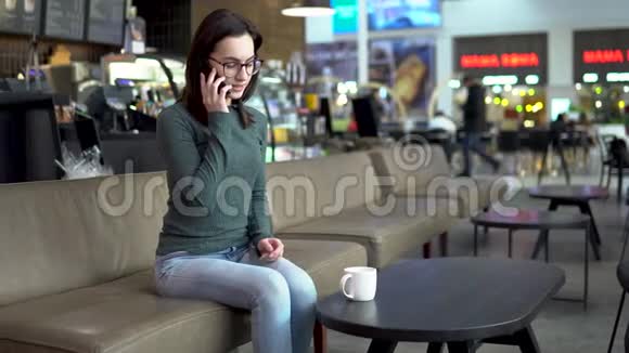 一个年轻的女人坐在咖啡馆里打电话一个女孩在打电话喝咖啡关闭视频的预览图