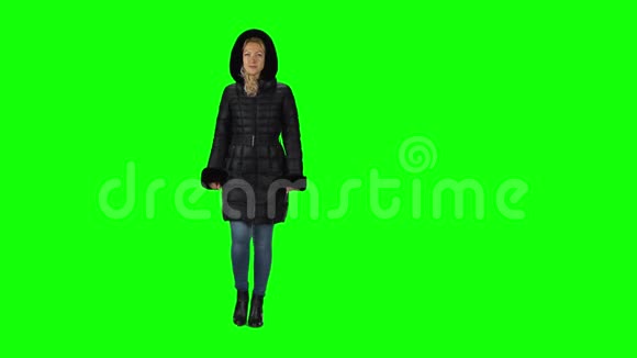 金发女孩穿着一件黑色的冬季外套头罩牛仔裤和靴子与绿色屏幕相衬视频的预览图