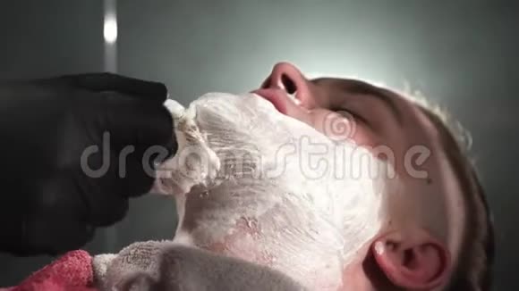 理发师用特殊的剃须膏涂在客户的脸上并将用危险的剃须刀刮胡子光在背后闪耀视频的预览图