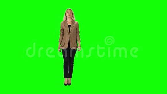 金发女孩穿着时尚的棕色夹克黑色裤子和高跟鞋穿着绿色的屏幕视频的预览图